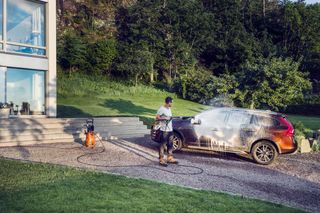 A person using a pressure washer to clean a car in a residential driveway.