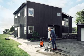 Eine Person, die einen Hochdruckreiniger benutzt, um einen Steinweg vor einem modernen Haus zu reinigen.