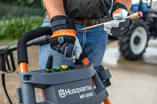 A person adjusting the nozzle on a Husqvarna HP 3000 pressure washer outdoors.