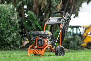A Husqvarna pressure washer positioned on a grassy area with construction equipment in the background.
