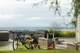 Een persoon die een fiets schoonmaakt met een tuinslang in een achtertuin.