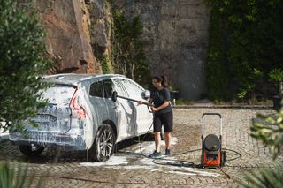 Husqvarna PW 370. Une personne utilise un nettoyeur haute pression pour nettoyer une voiture en extérieur.