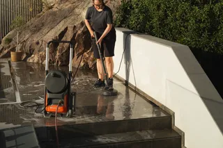 En person som städar en våt stenuteplats med en golvskurare.