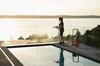 En person som använder en högtryckstvätt för att rengöra ett glasstaket vid en pool vid solnedgången.