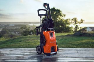 A Husqvarna pressure washer standing on a wooden deck with a scenic background.