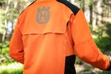 Person, die in einer Waldumgebung eine Husqvarna Arbeitsjacke trägt.