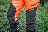 Close-up of Husqvarna chainsaw trousers worn by a person in a forest setting.