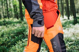 Person wearing Husqvarna work trousers in a forest setting.