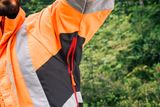 Крупний план людини в робочому одязі з логотипом Husqvarna, яка стоїть у лісі.