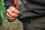 Primo piano di una persona che regola la coulisse sui pantaloni da lavoro all'aperto.