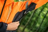 Una persona che regola la cerniera sulla manica di una giacca da lavoro Husqvarna in un ambiente forestale.