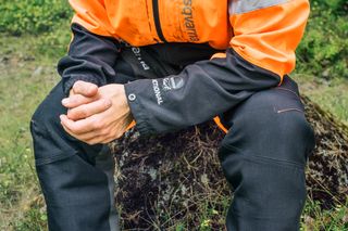 Person sitting on a rock wearing Husqvarna work gear in an outdoor setting.