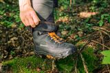 A person adjusting Husqvarna work boots in a forest setting.