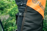 Close-up of a person wearing Husqvarna chainsaw trousers in a garden setting.