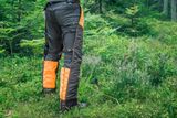 Person facing away wearing chainsaw trousers in a forest setting.