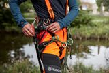 A person wearing Husqvarna work gear with climbing equipment near a water body.