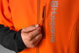 Primer plano de una persona subiendo la cremallera de una chaqueta Husqvarna, mostrando el logotipo de la marca.