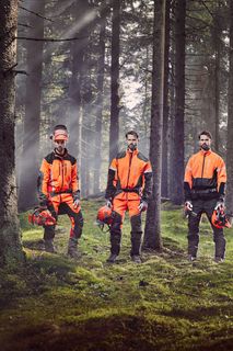 Četvero ljudi u radnoj opremi stoji u šumi držeći kacige i motorne pile.