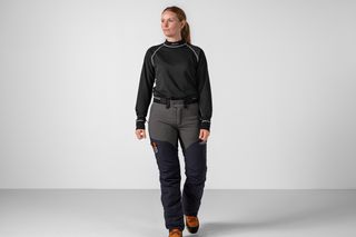 Person som bär arbetskläder, inklusive skyddsbyxor och stövlar, går framåt.