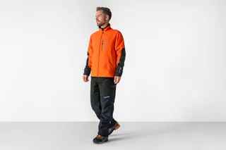 Persona que lleva ropa de trabajo, incluyendo una chaqueta y pantalones, de pie en un estudio.