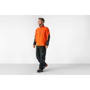 Persona que lleva ropa de trabajo, incluyendo una chaqueta y pantalones, de pie en un estudio.