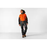 Asmuo, dėvintis darbo aprangą, įskaitant striukę ir kelnes, stovintis studijoje.