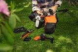 A person putting a Husqvarna battery pruner on a pole on a grassy area.