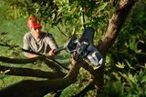 Una persona con una motosierra para cortar ramas de árboles en un jardín.