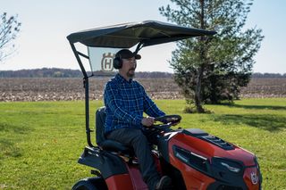 A person driving a ride-on mower with a canopy in a field setting.
