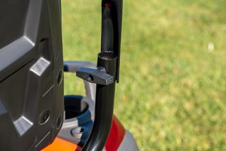 Close-up of a lawn mower handle and part of the machine, set against a grassy background.