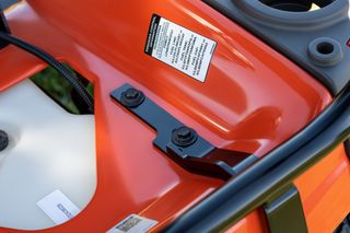 Close-up of a lawn mower's deck with bolts and a warning label.