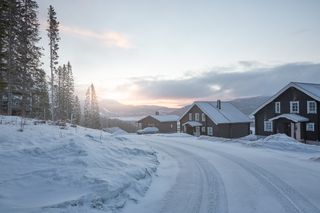 Snødekt landskap med hus og trær ved solnedgang.