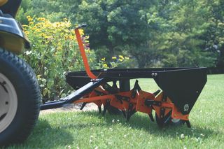 A lawn aerator attached to a ride-on mower, used for soil cultivation in a garden.