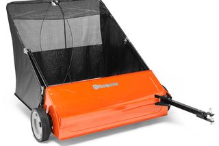 Side view of a Husqvarna lawn sweeper with a detachable bag and tow bar.