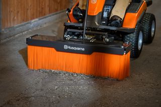 Une tondeuse autoportée Husqvarna équipée d’un accessoire de balayage pour nettoyer un sol en béton.