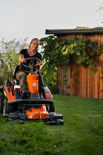 Een persoon die gazon maait met een zitmaaier in een tuinomgeving.
