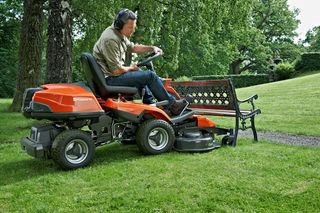 En person, der betjener en havetraktor i en have, nær en træbænk.