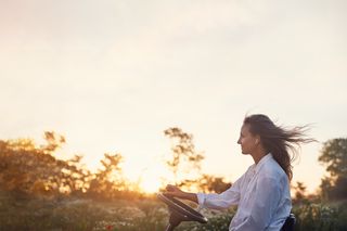 En person som kjører gressklipper på et jorde i solnedgangen.