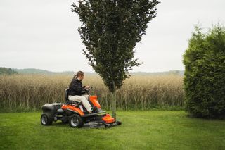 En person, der slår græs med en havetraktor i en haveindstilling.