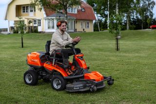O persoană care tunde gazonul cu o mașină de tuns iarba într-o grădină.