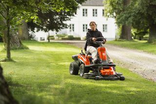 En person som klipper gräset med en åkgräsklippare i trädgårdsmiljö.