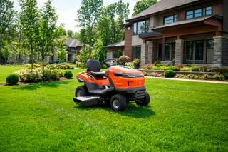 Husqvarna ride-on lawn mower parked on a manicured lawn in front of a modern house.
