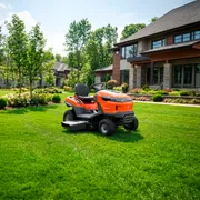 Husqvarna ride-on lawn mower parked on a manicured lawn in front of a modern house.
