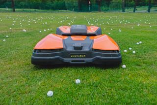 Robotic lawn mower operating on a golf course with scattered golf balls.
