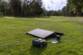 Mähroboter auf einer Wiese mit einer Solarmodul-Ladestation.