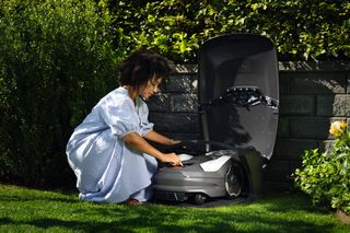 A person interacting with a robotic lawn mower in a garden setting.