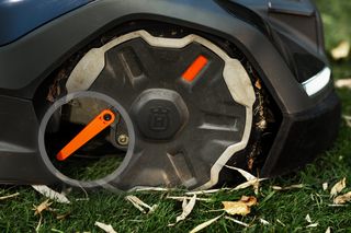 Close-up of a robotic lawn mower on grass with fallen leaves.