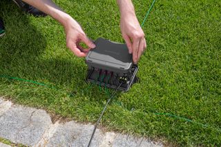 A person installing a Husqvarna robotic lawn mower charging station on a lawn.