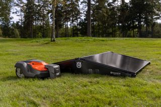 Husqvarna Mähroboter neben einer Solarladestation auf einer Wiese.