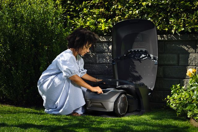 A person placing a robotic lawn mower into its charging station in a garden.